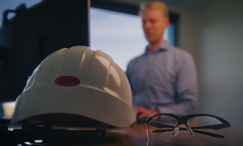 Construction helmet and protective glasses on the desk of the occupational health and safety manager that reads an occupational health and safety white paper. 